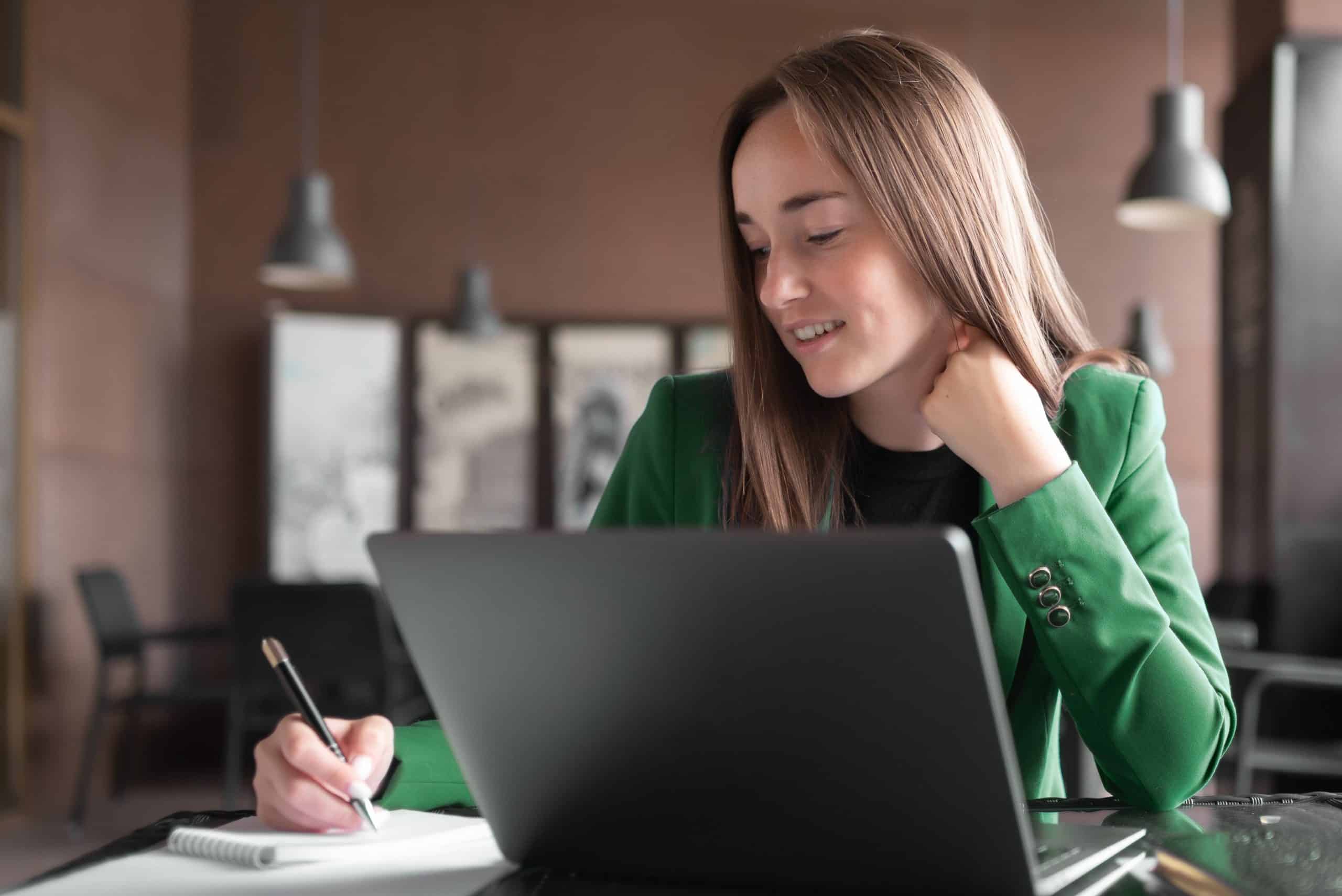 A lady attending a capital markets course online using her laptop and making valuable notes